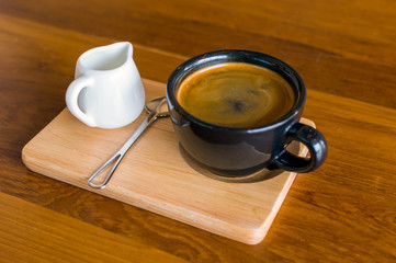 Dark black blue coffee cup with americano coffee, spoon and a milk jug on a wooden stand