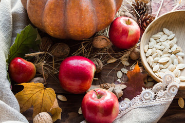 Naklejka na ściany i meble Autumn orange pumpkin, red apples, walnuts, acorns and dry foliage on a wooden background