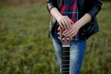  girl stands with a guitar without playing, strings at rest, laying her hands on the pegs and holding it in front of her