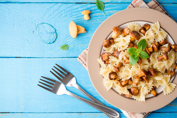 Farfalle pasta with chanterelles and basil on blue wooden table