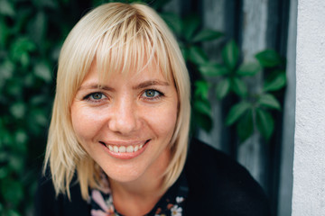 Fototapeta premium Close up portrait of smiling Cute young blonde beautiful stylish woman in pretty blouse in flowers and black cardigan over green grape leaves background.