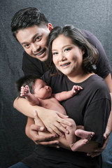 family portrait of young asian mum and dad and boy newborn in black background .