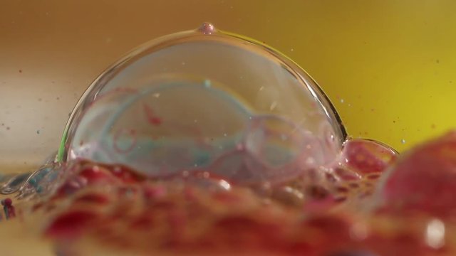 Colorful bubble on water pops in slow motion, close up