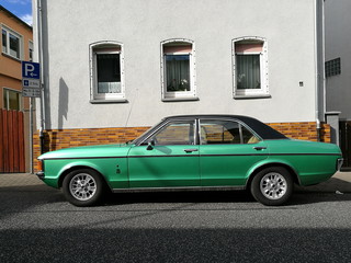 Grüne viertürige Limousine der Siebzigerjahre mit schwarzem Vinyldach im Sommer bei Sonnenschein...