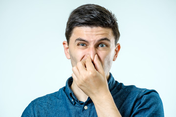 Man holding his nose against a bad smell over gray background