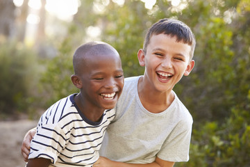 Portrait of two boys embracing and laughing hard outdoors - obrazy, fototapety, plakaty