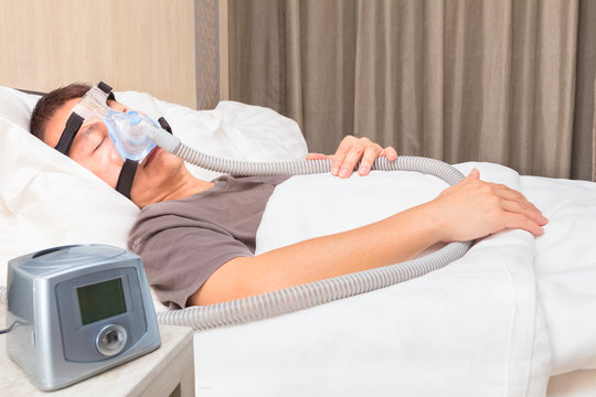 middle age asian man sleeping in bed wearing CPAP mask connecting to air hose and CPAP machine, device for people with sleep apnea