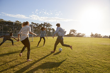 Four young adults playing football in a park at sunset