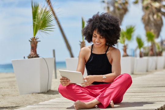 Happy afro american woman sitting crossed legs using tablet - Powered by Adobe