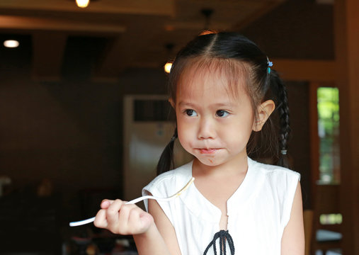 Close up Asian kid girl eating delicious food on table for lunch in the restaurant, Holding plastic fork in her hand.