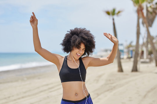 Happy afro american woman listening music dancing on beach