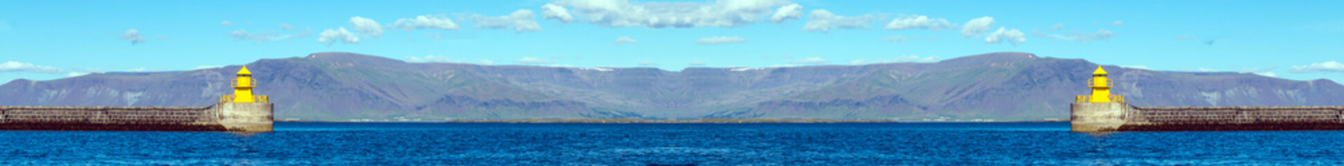 Yellow lighthouse in ocean bay against blue sky and mountains on horizon. Copy space. Leaderboard. Wide panoramic image.