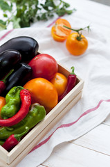 Fresh vegetables, tomatoes, peppers, aubergines, chilli pepper in a wooden box in the open air. Vegetable background.
