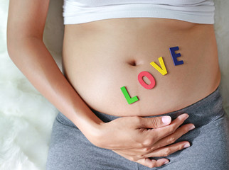 Close up Pregnant woman sitting on soft sofa and touching her belly with sign LOVE in front of her belly.
