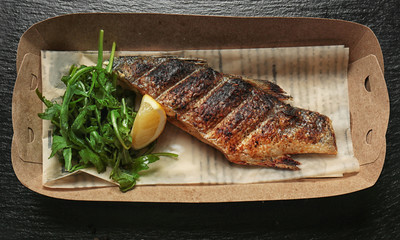 Cardboard box with delicious fish and arugula on table