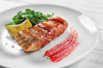 Plate with delicious fish in bacon and arugula on table