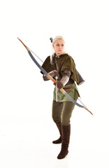 full length portrait of a blonde girl wearing green and brown medieval costume, holding a bow and arrow. isolated on white background.