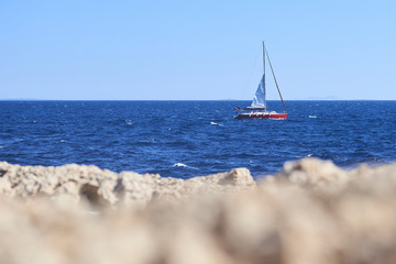 Yacht Sailing on the blue Sea with rocks foreground