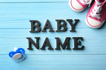 Text BABY NAME, pacifier and shoes on color wooden background