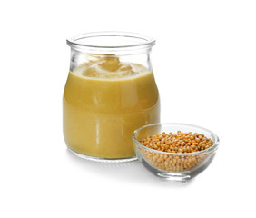 Mustard seeds in bowl and jar with delicious sauce on white background