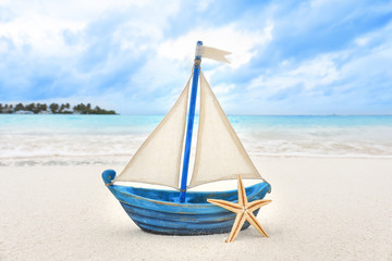 Obraz premium Small toy ship and starfish on sea beach. Summer vacation concept