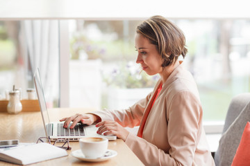 Cheerful business woman in the cafe typing on laptop with coffee and dairy