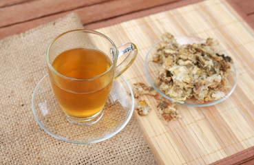 Chrysanthemum juice in glass cup and dried Chrysanthemum flower on wood background against green grass background.