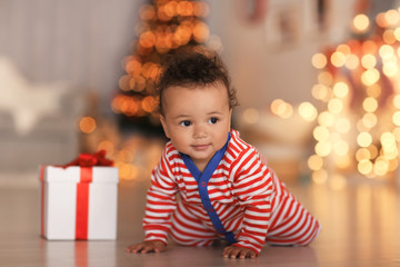 Fototapeta na wymiar Cute little baby with gift box on floor and blurred Christmas lights on background