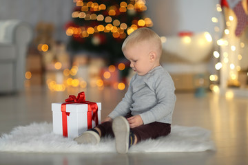 Fototapeta na wymiar Cute little boy with gift box sitting on floor in decorated for Christmas room