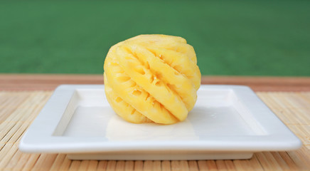 Pineapple fruit in ceramic plate on wooden table.