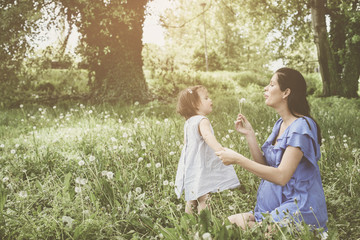 Pregnant mother playing with little daughter in park. Mother and daughter blowing dandelion.