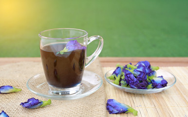 Butterfly pea juice in transparent glass and flowers on wooden plank background.