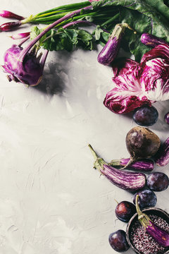 Assortment raw organic of purple vegetables mini eggplants, spring onion, beetroot, radicchio salad, plums, kohlrabi, flower salt over gray concrete background. Top view with space. Food frame