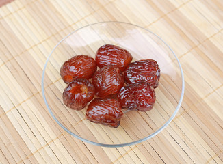 Jujube coated with syrup in plate against wooden background. Chinese date.