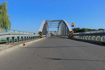 Grey steel bridge across the Narew river in Tykocin, Poland on a sunny day with clear blue sky