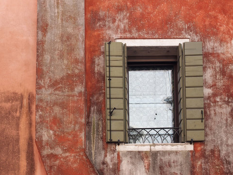 ancient building in venice with red faded painted wall and green shutters on a window