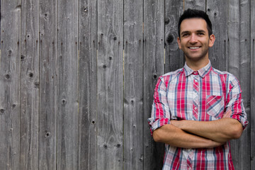 Obraz premium Portrait of handsome young man in shirt keeping arms crossed and smiling while standing against wooden background.