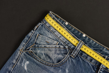 Jeans with yellow measure tape used as belt, close up