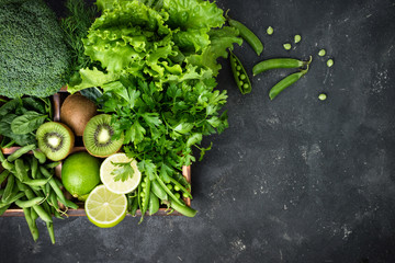 Green vegetables background. Fresh garden produce. Broccoli, spinach, kiwi, lettuce, parsley, dill, asparagus beans on dark concrete table, top view and copy space