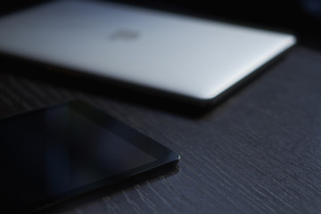 Close-up of a tablet lying on a dark desk next to the laptop