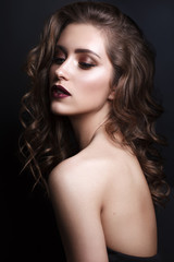 Fototapeta premium Portrait of beautiful young woman with professional makeup, perfect skin, red lips, volume wavy hairstyle on dark background. Trendy bronze smoky eyes.