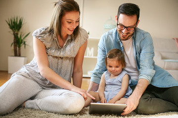 Family lying on the floor with their baby. Family using digital tablet together on the floor.
