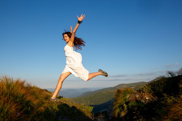 Beautiful woman in white dress running in the mountains. Jumping on mountain peak rock. Beautiful girl looking happy and smiling. Relaxing, feeling alive, breathing fresh air, got freedom from work