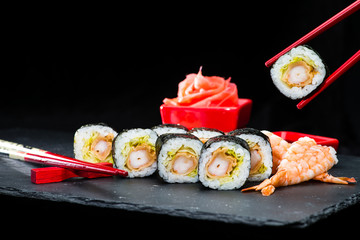 traditional Japanese cuisine. Process of eating sushi rolls with cream cheese, rice, maki, avocado and shrimp on dark background, selective focus