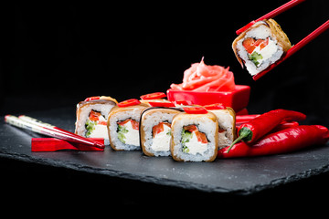 traditional Japanese cuisine. Process of eating sushi rolls with salmon, cream cheese, rice, chili pepper and cucumber on dark background, selective focus