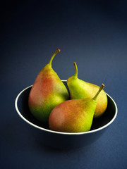 Healthy organic pears in blue bowl on blue background.