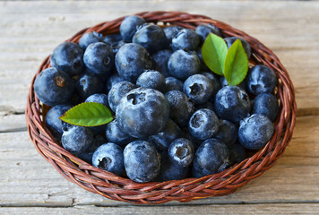 Freshly picked blueberries in a basket on old wooden background.Fresh blueberries with green leaves on rustic table. Blueberry. Bilberry.Healthy eating,diet and nutrition concept.