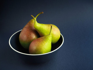 Healthy organic pears in blue bowl on blue background.
