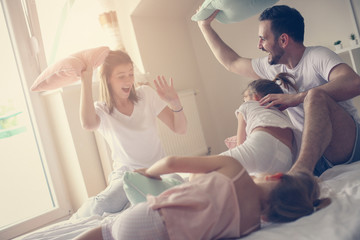 Family having funny pillow fight on bed. Parents spending free time with their daughters. Fight...