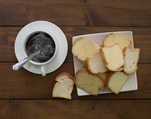 Crispy buns in white dish with hot black coffee on wooden dark background